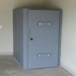 Gray, prefabricated steel storm shelter, installed above ground in a backyard.
